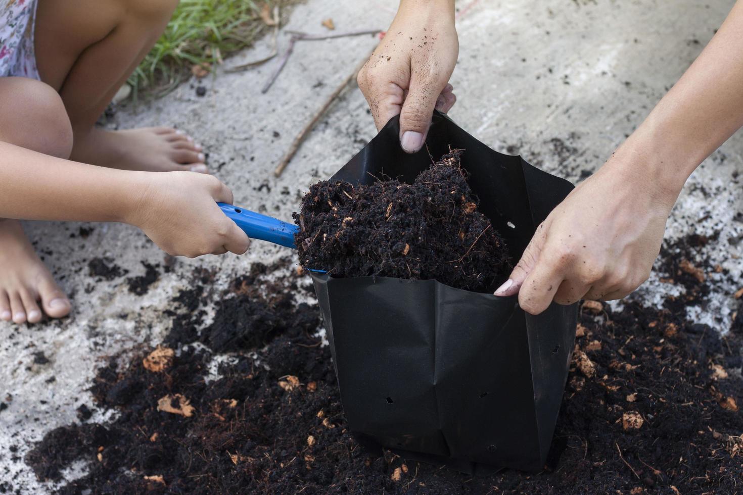 mano della figlia che tiene una pala per aiutare il padre a raccogliere il terreno mescolato con polvere di cocco e mettere in un sacchetto di plastica nera per la scuola materna. foto