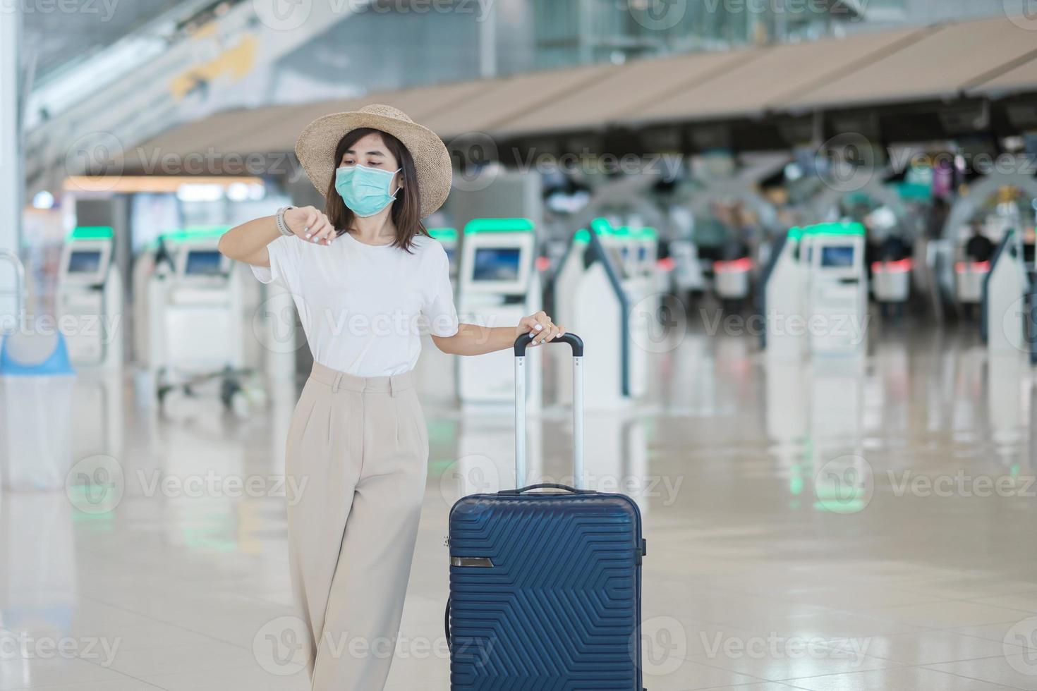 giovane donna che indossa una maschera facciale con bagagli che camminano in aeroporto, protezione da infezione da coronavirus, viaggiatore asiatico con cappello. tempo di viaggiare dopo il concetto di dose di richiamo del vaccino foto