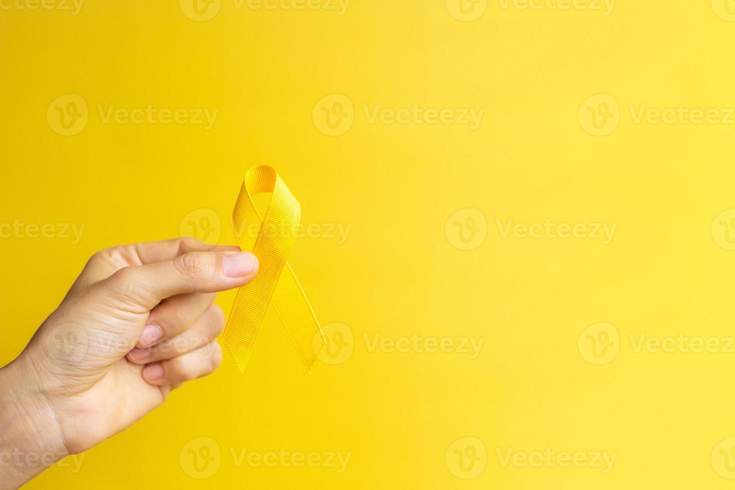 mano che mostra un nastro giallo su sfondo giallo per sostenere le persone che vivono e le malattie. giornata di prevenzione del suicidio di settembre, mese di sensibilizzazione sul cancro infantile e concetto di giornata mondiale del cancro foto