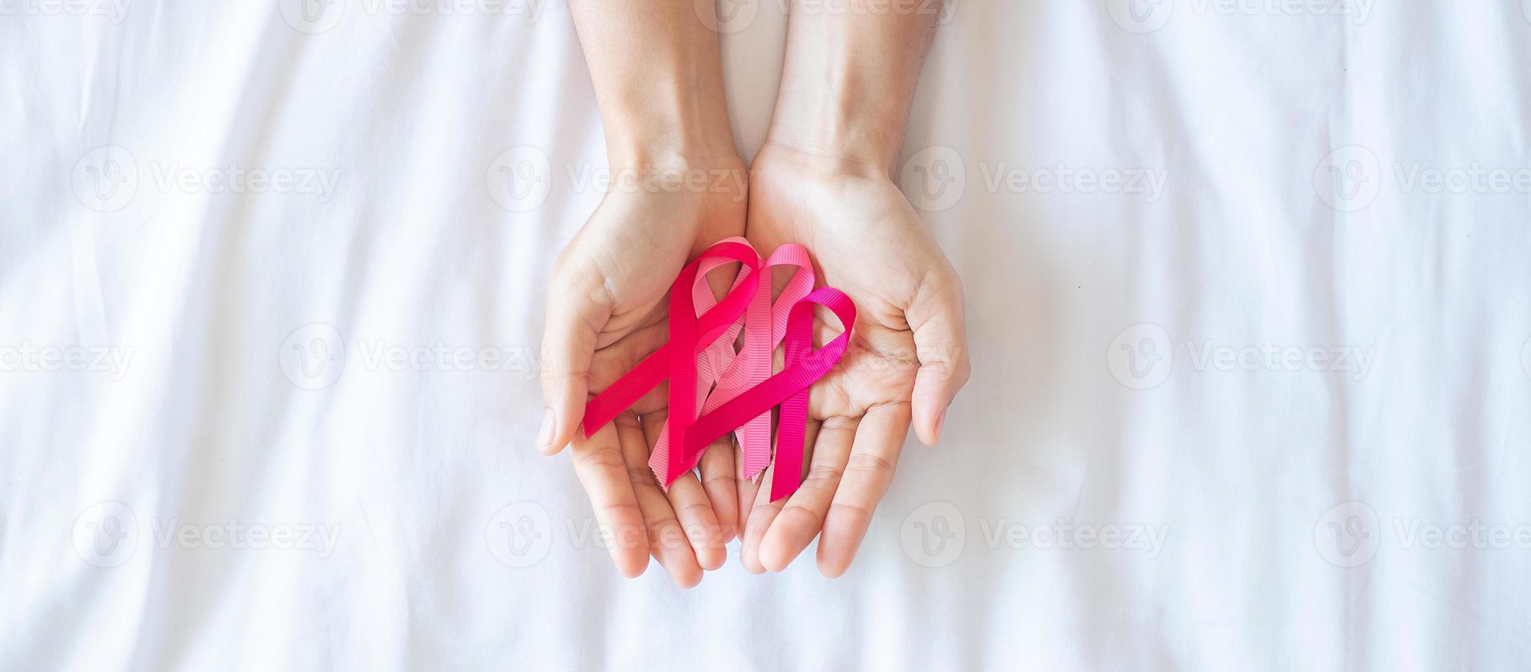 mese di sensibilizzazione sul cancro al seno di ottobre, mano di donna adulta che tiene nastro rosa su sfondo rosa per sostenere le persone che vivono e le malattie. concetto internazionale delle donne, della madre e della giornata mondiale del cancro foto