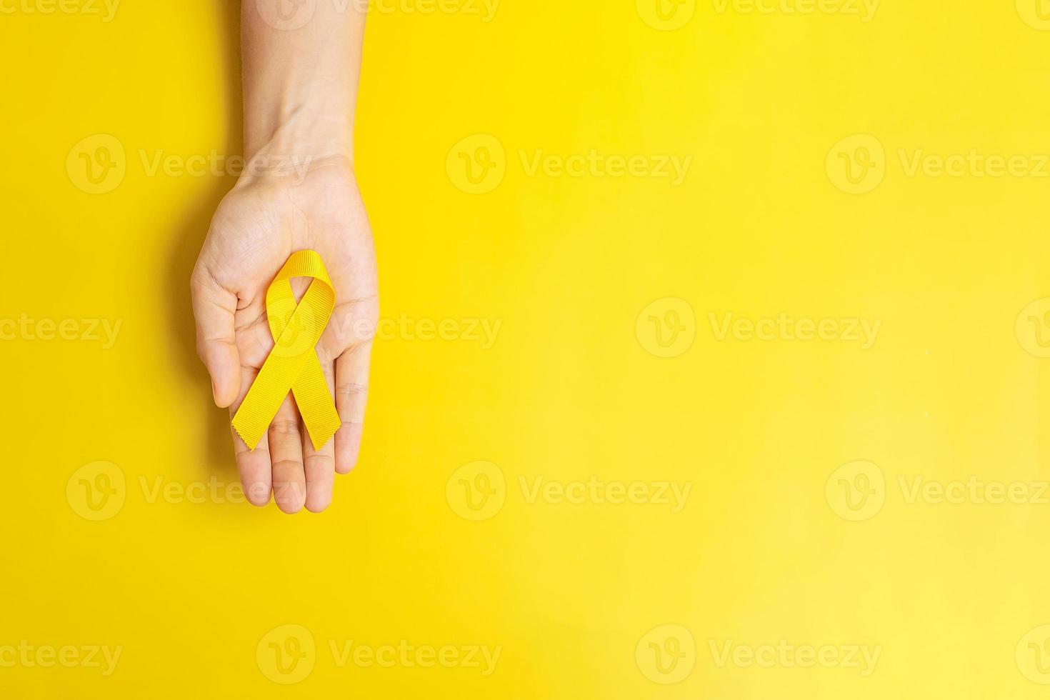 mano che tiene un nastro giallo su sfondo giallo per sostenere le persone che vivono e le malattie. giorno di prevenzione del suicidio, cancro del sarcoma e concetto di mese di sensibilizzazione sul cancro infantile foto