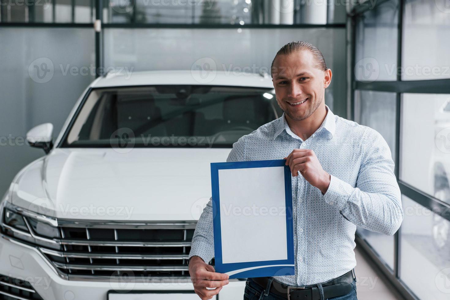 sorridente e di buon umore. manager si trova di fronte a una moderna auto bianca con carta e documenti in mano foto