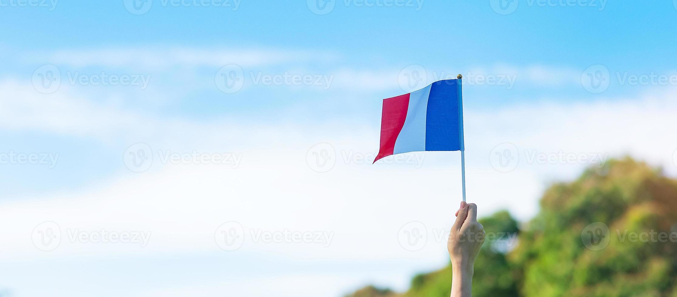 mano che tiene la bandiera della francia su sfondo blu cielo. festa della festa nazionale francese, giorno della bastiglia e felici concetti di celebrazione foto