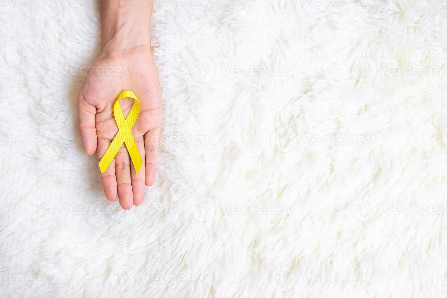 mano che tiene il nastro giallo su sfondo bianco per sostenere le persone che vivono e le malattie. giornata di prevenzione del suicidio di settembre, mese di sensibilizzazione sul cancro infantile e concetto di giornata mondiale del cancro foto