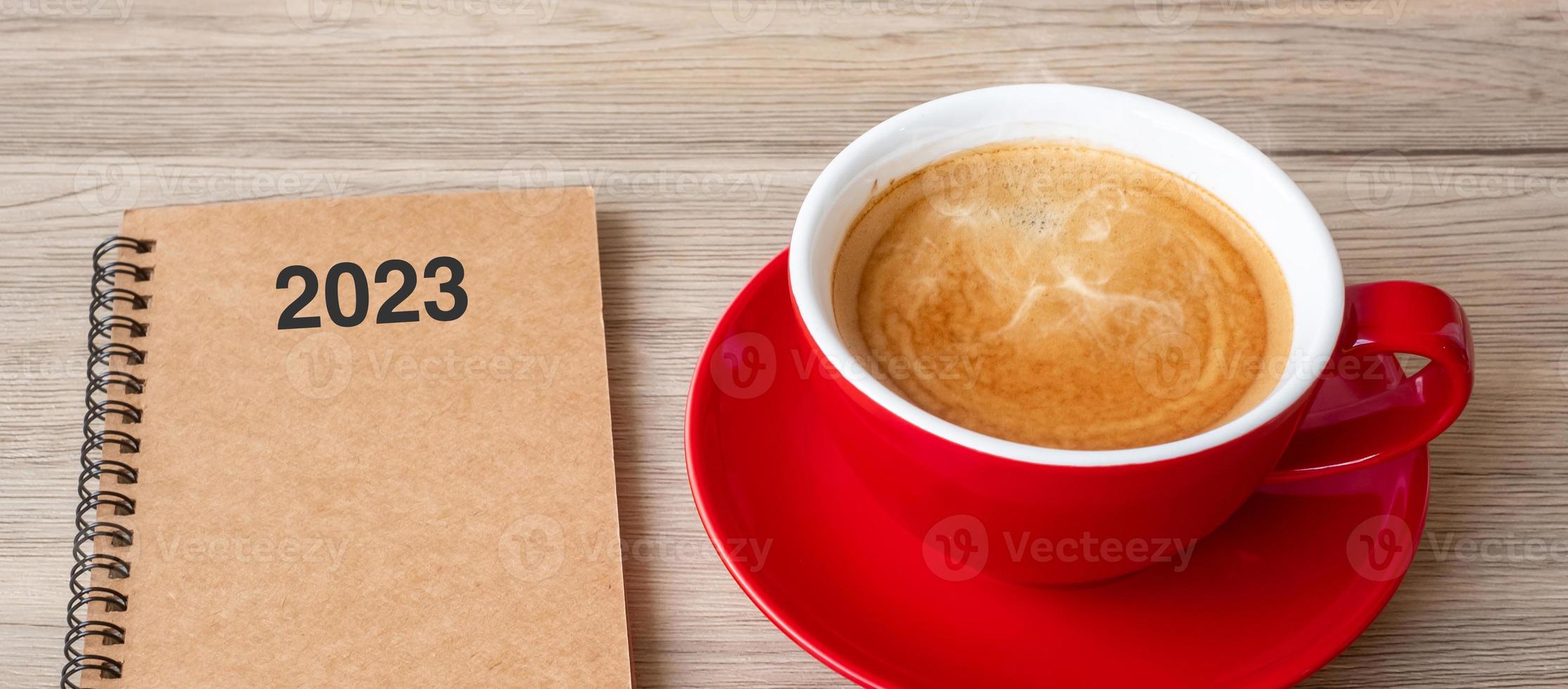 taccuino 2023 e tazza di caffè su tavolo di legno, vista dall'alto e spazio per la copia. natale, felice anno nuovo, obiettivi, risoluzione, elenco delle cose da fare, strategia e concetto di piano foto