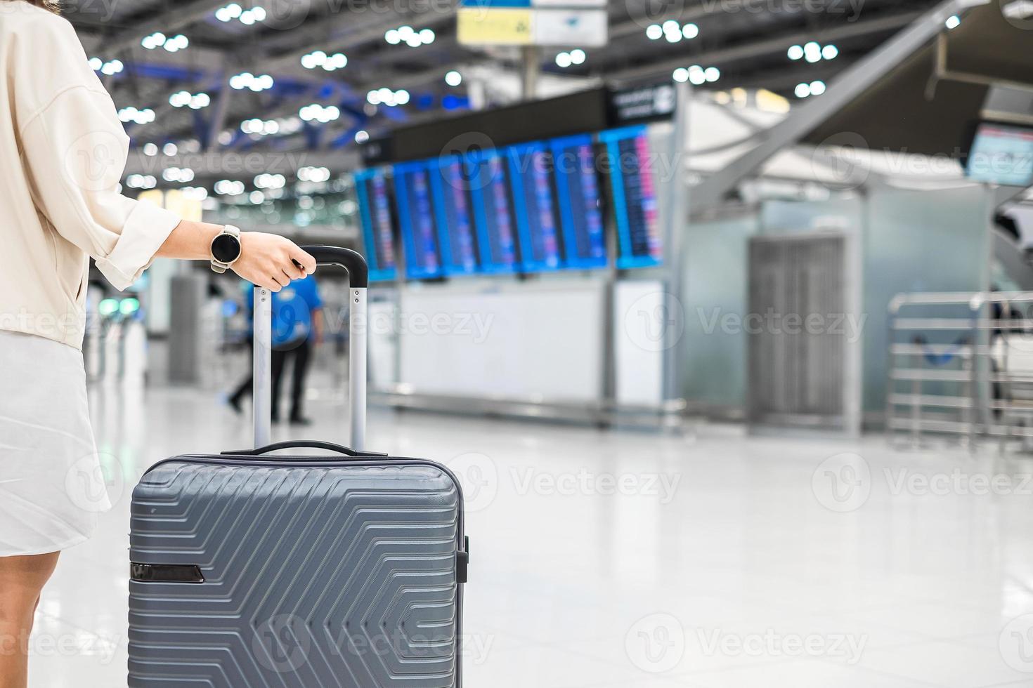 maniglia del bagaglio della holding della mano della giovane donna prima di controllare l'orario di volo in aeroporto, trasporti, assicurazione, viaggi e concetti di vacanza foto