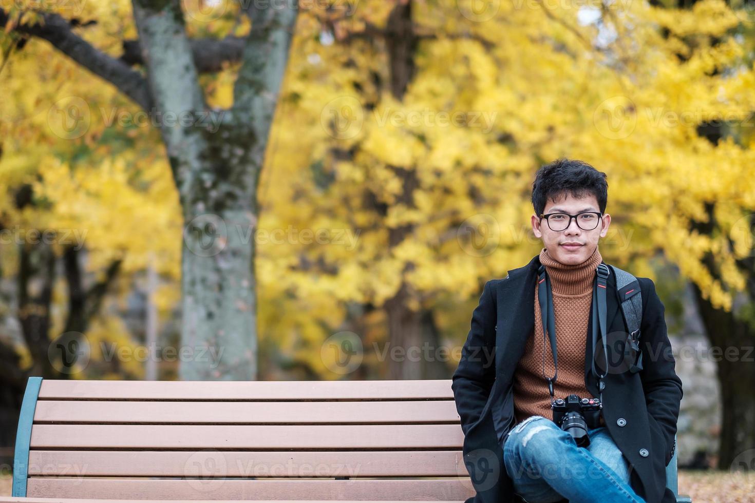 l'uomo felice si diverte al parco all'aperto nella stagione autunnale, viaggiatore asiatico in cappotto e macchina fotografica su sfondo giallo foglie di ginkgo foto