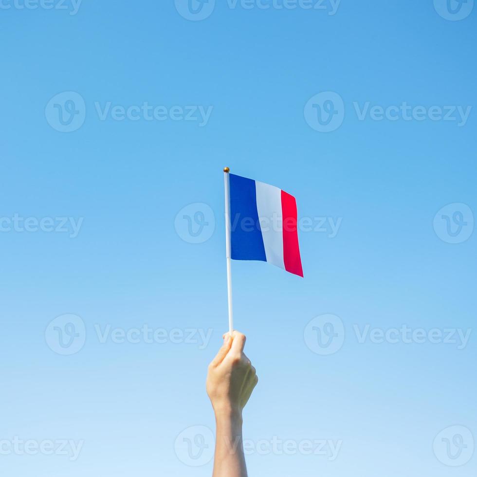 mano che tiene la bandiera della francia su sfondo blu cielo. festa della festa nazionale francese, giorno della bastiglia e felici concetti di celebrazione foto