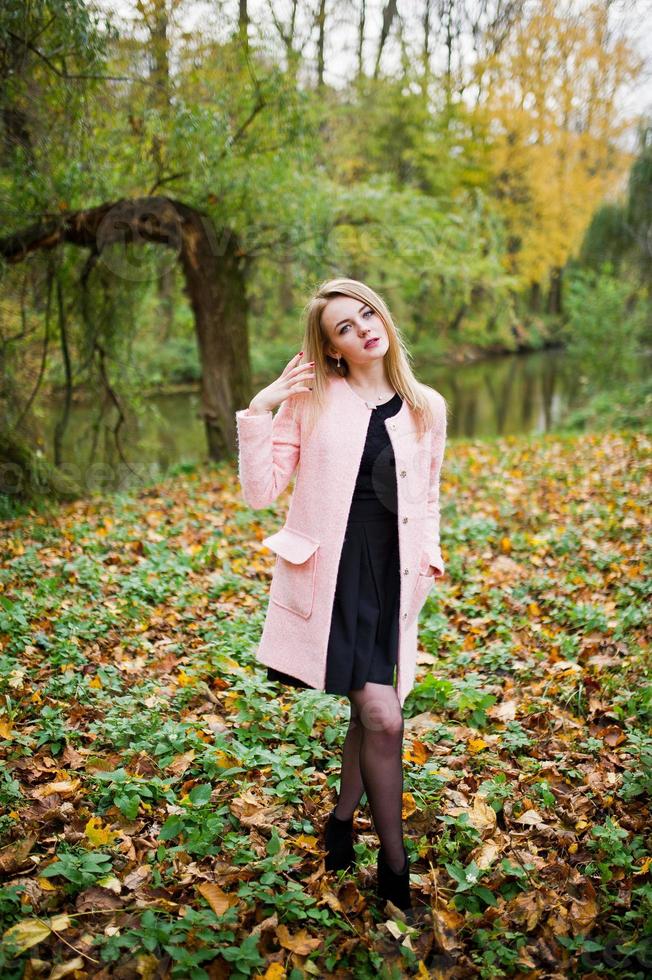 giovane ragazza bionda al cappotto rosa posato sul parco autunnale. foto