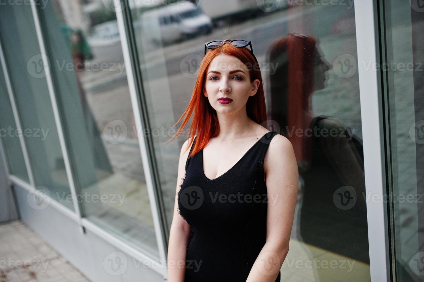 ragazza alla moda dai capelli rossi in occhiali da sole indossano in nero, contro grandi finestre. ritratto di moda di strada. foto