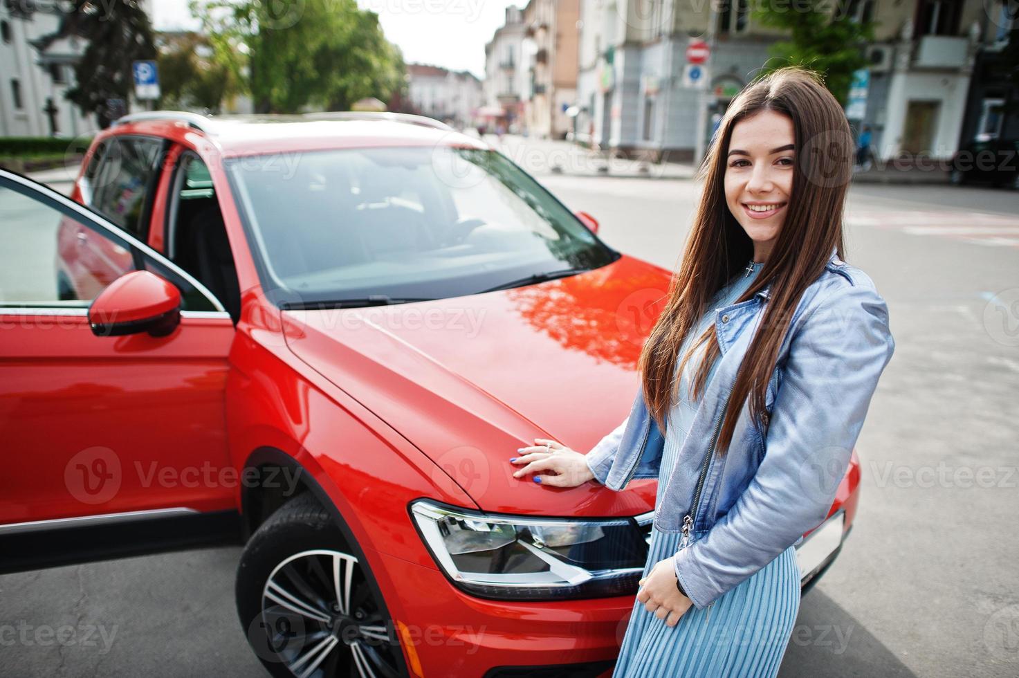 foto all'aperto di una splendida donna in posa vicino a un'auto suv arancione.