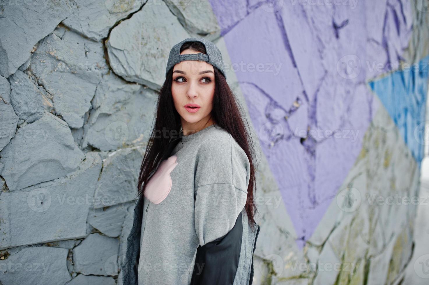 elegante ragazza bruna con berretto grigio, casual street style in giornata invernale contro il muro colorato. foto