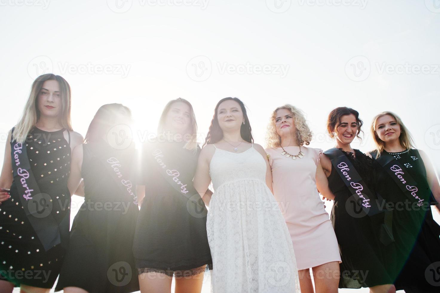 un gruppo di 7 ragazze indossano il nero e 2 spose alla festa di addio al nubilato contro la spiaggia soleggiata. foto