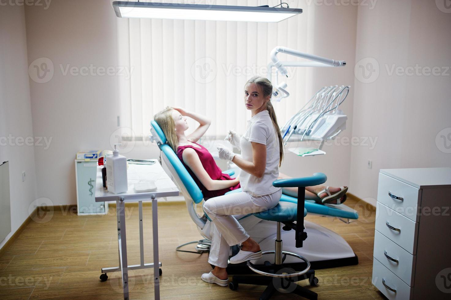 paziente attraente in abito rosso-viola sdraiato sulla poltrona del dentista mentre il dentista femminile si cura i denti con strumenti speciali. foto