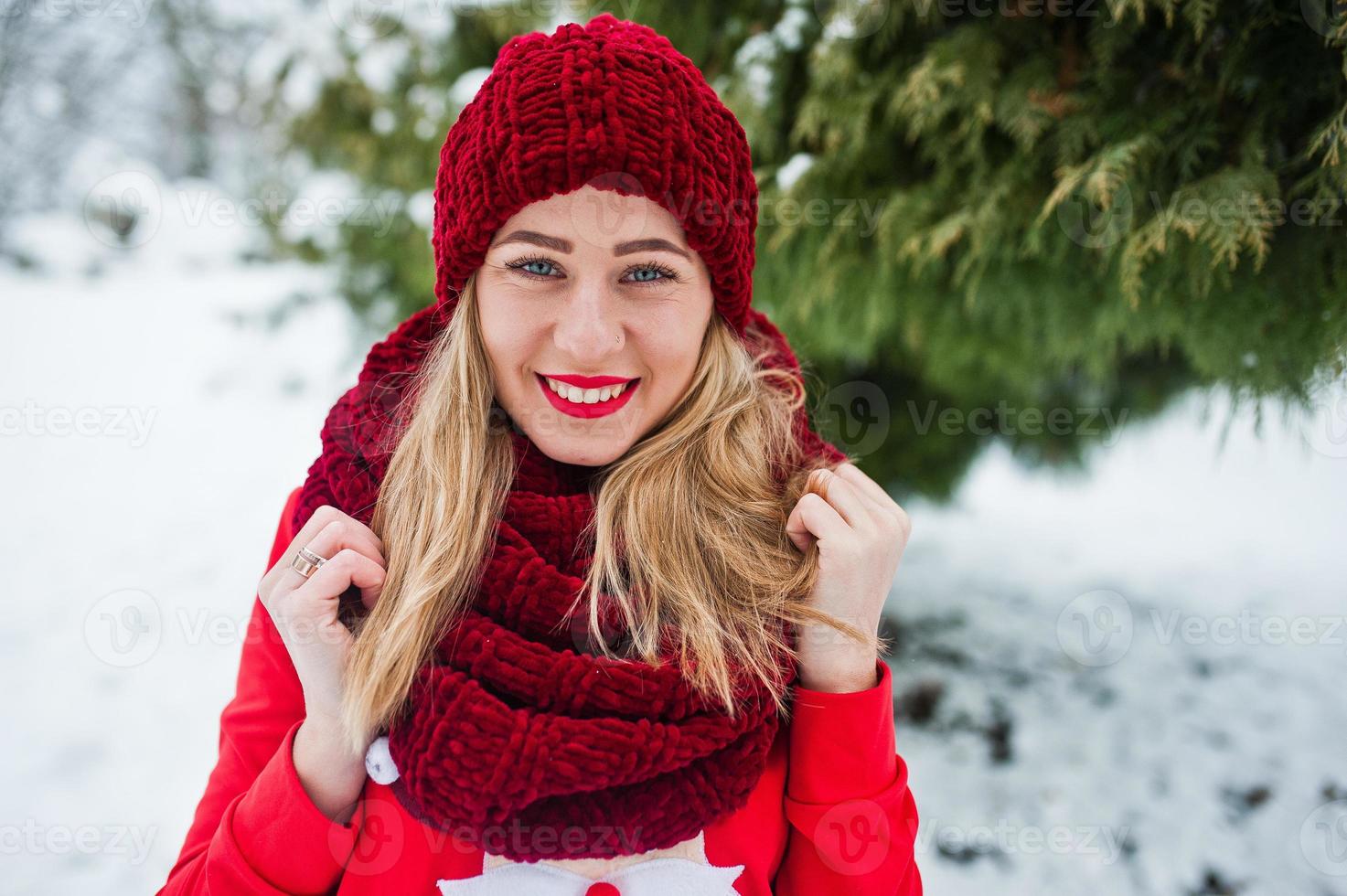 ragazza bionda in sciarpa rossa, cappello e maglione di Babbo Natale in posa al parco il giorno d'inverno. foto