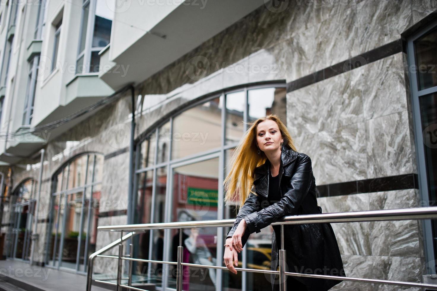 bionda ragazza alla moda in lungo cappotto di pelle nera poste alla ringhiera di ferro. foto