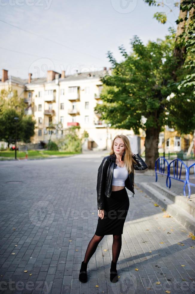 elegante ragazza bionda indossa una giacca di pelle nera in posa per le strade della città. foto