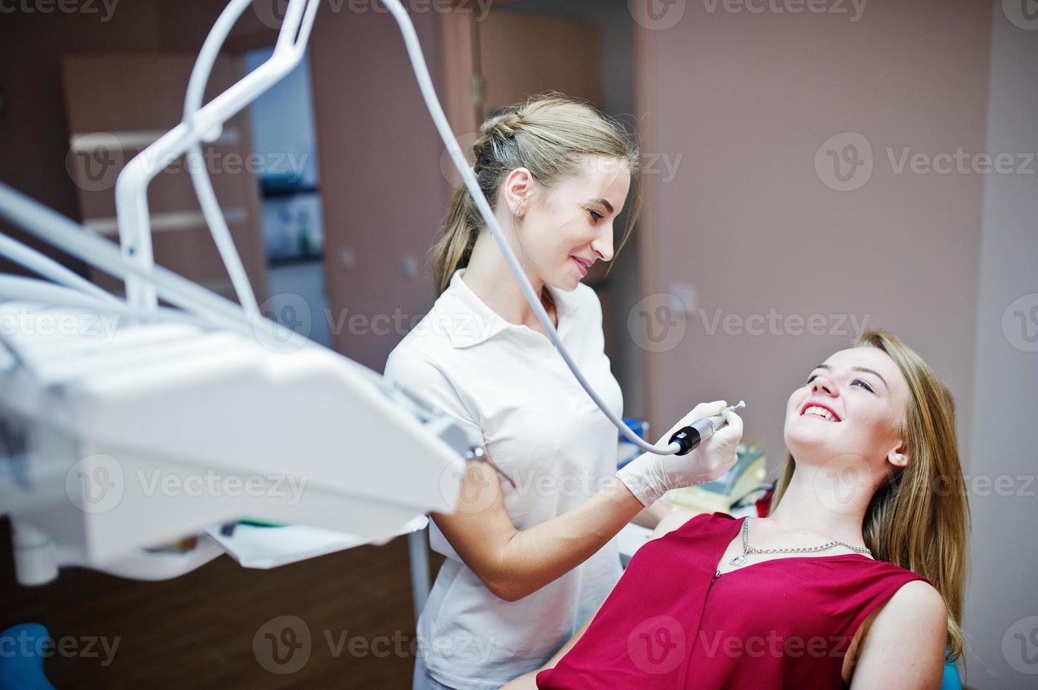 paziente attraente in abito rosso-viola sdraiato sulla poltrona del dentista mentre il dentista femminile si cura i denti con strumenti speciali. foto