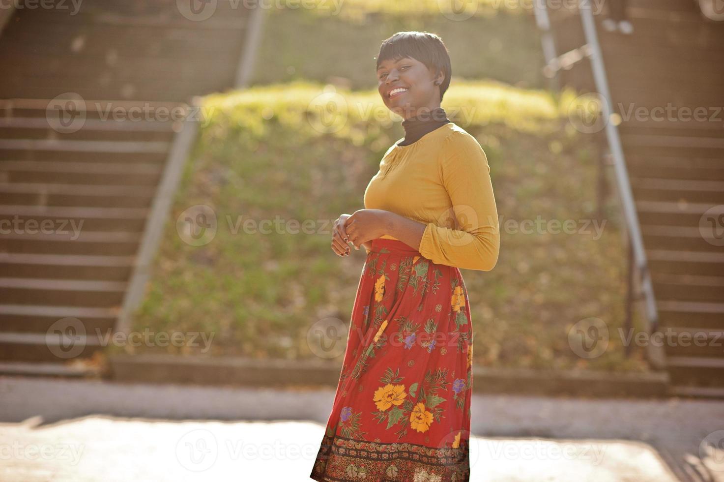 ragazza afroamericana in abito giallo e rosso al parco autunnale dorato. foto