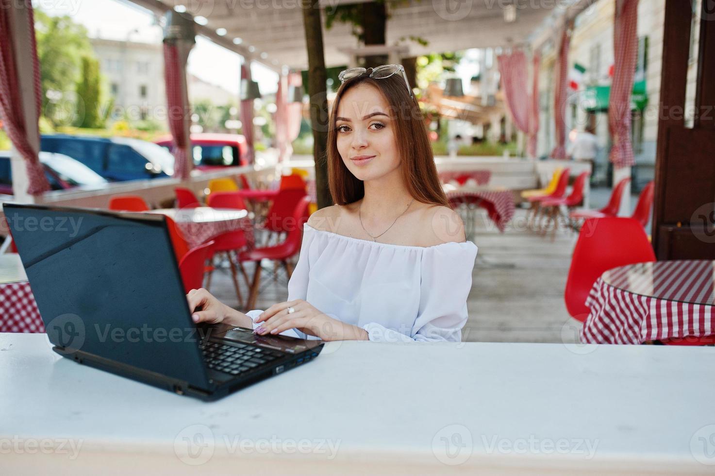 ritratto di una forte imprenditrice di successo indipendente che indossa abiti casual intelligenti e occhiali che lavorano su un laptop in un caffè. foto