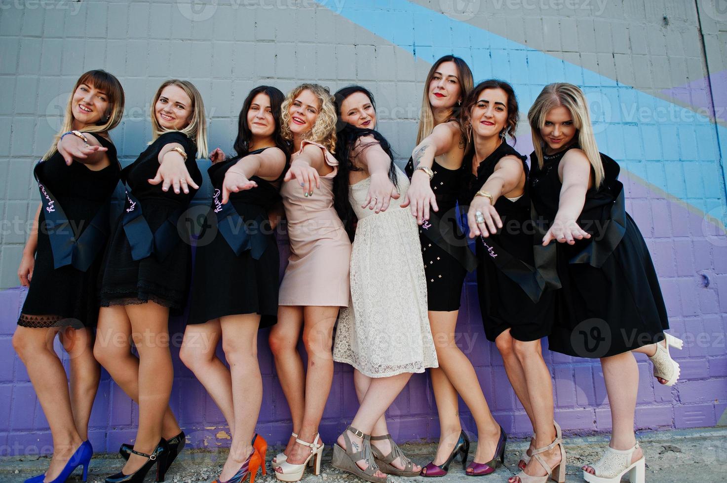 un gruppo di 8 ragazze indossano il nero e 2 spose all'addio al nubilato contro il muro colorato. foto