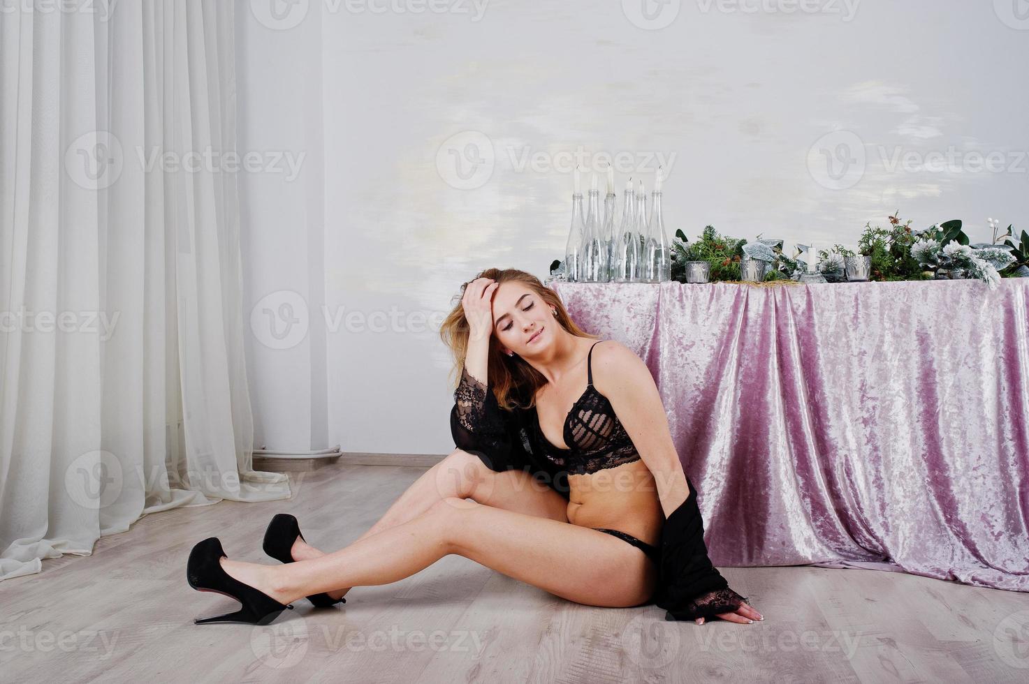 modella bionda sexy in lingerie nera e tacchi alti contro il tavolo con candele decorazioni natalizie. foto