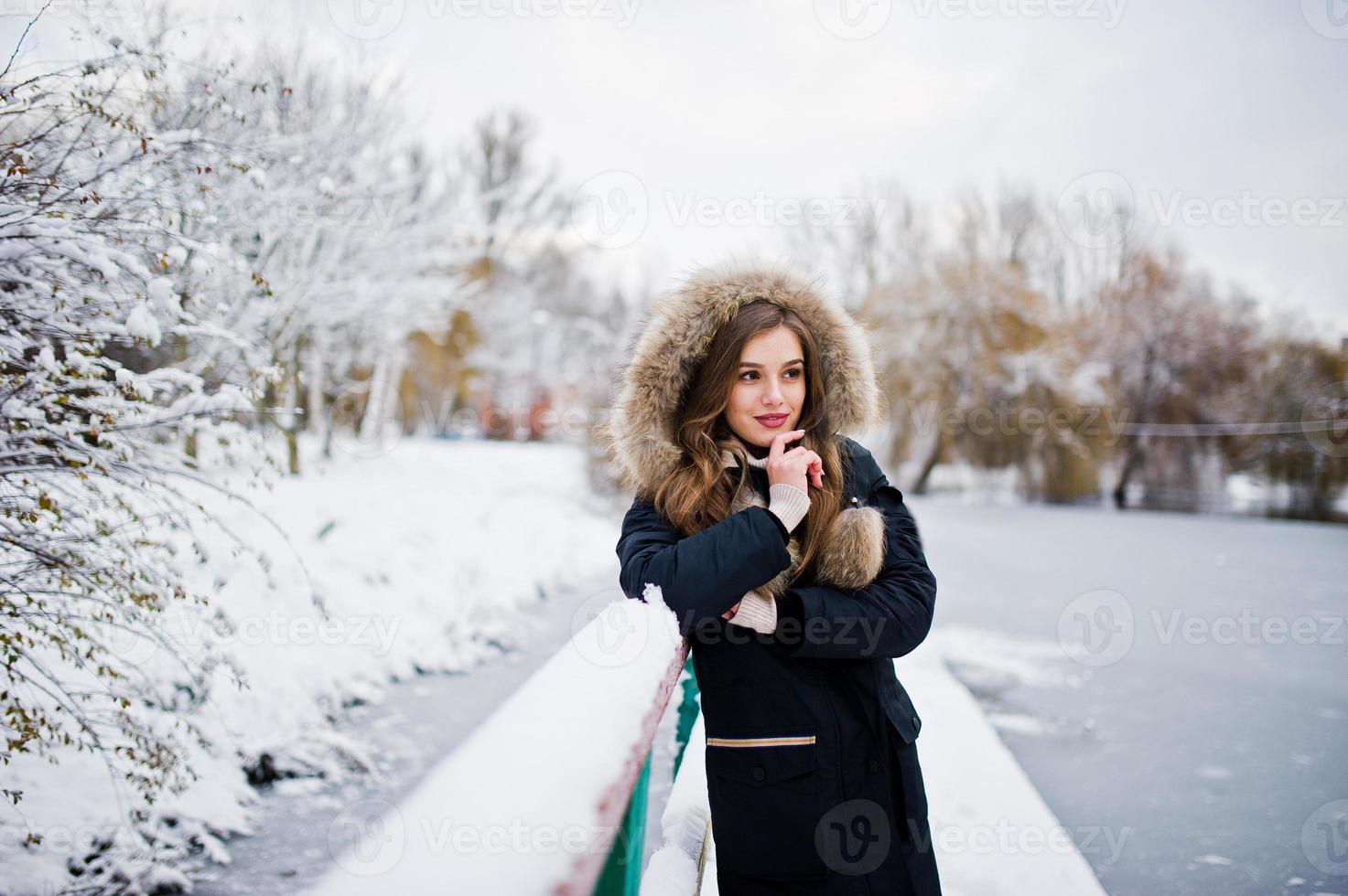 bella ragazza bruna in abiti caldi invernali. modello su giacca invernale contro il lago ghiacciato al parco. foto
