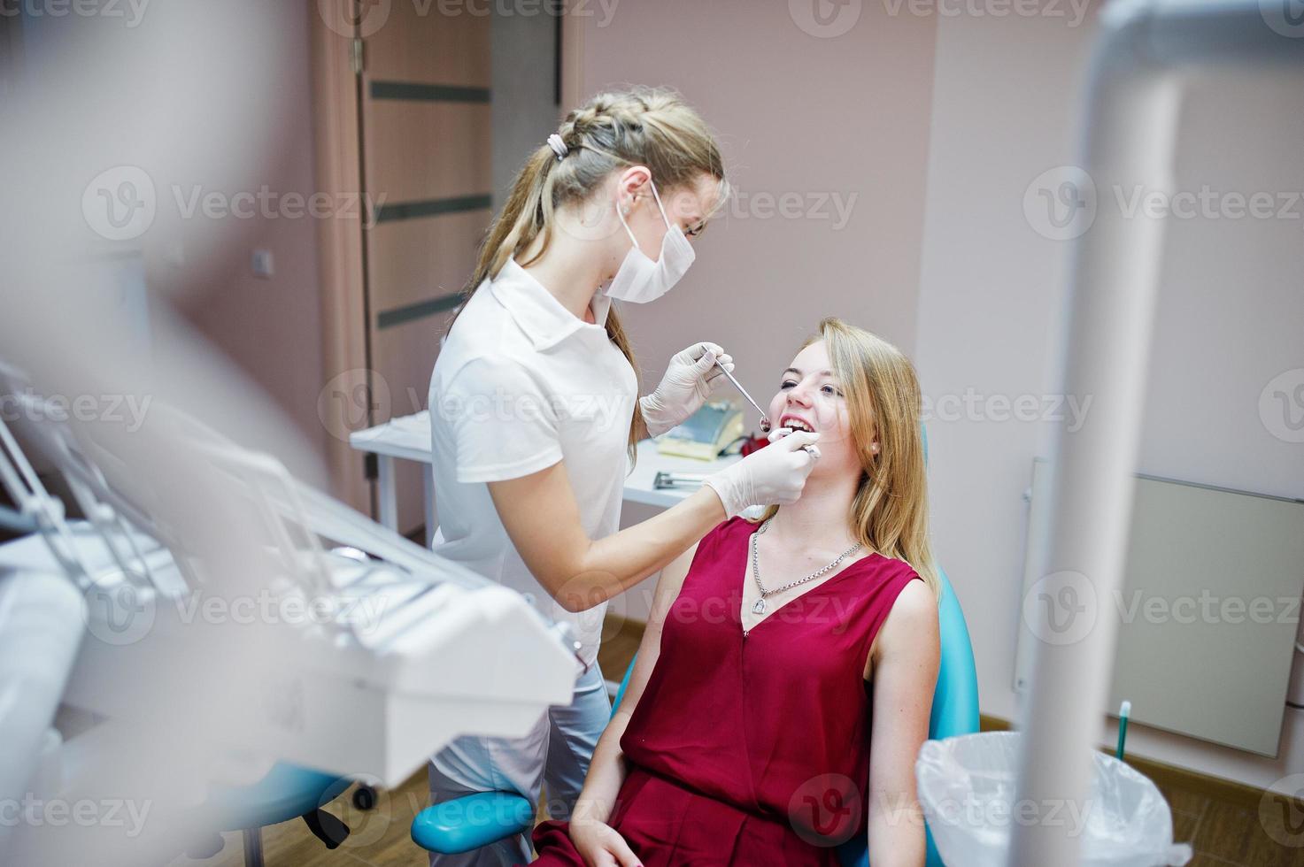 paziente attraente in abito rosso-viola sdraiato sulla poltrona del dentista mentre il dentista femminile si cura i denti con strumenti speciali. foto