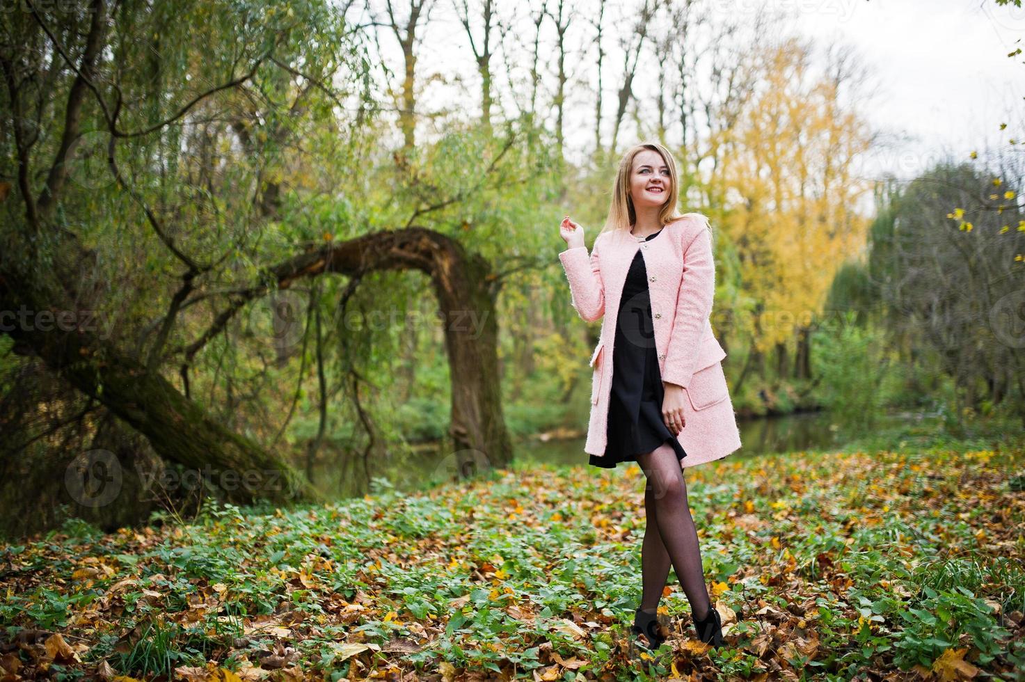 giovane ragazza bionda al cappotto rosa posato sul parco autunnale. foto