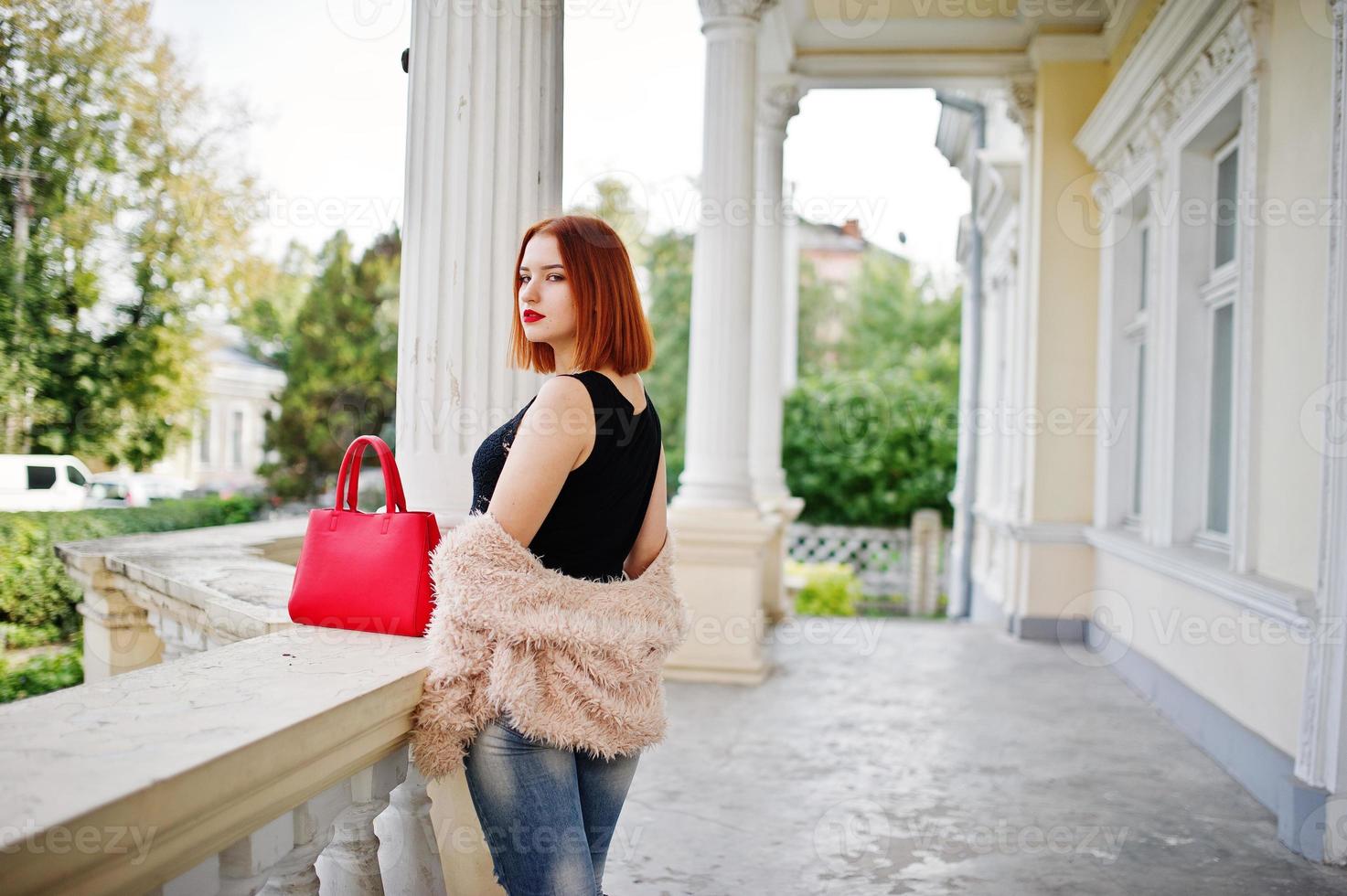 ragazza dai capelli rossi con borsa rossa posata vicino a casa d'epoca. foto