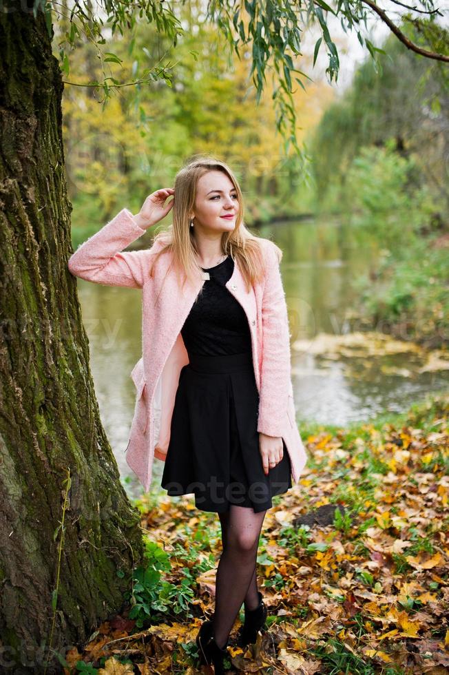 giovane ragazza bionda al cappotto rosa posato sul parco autunnale. foto