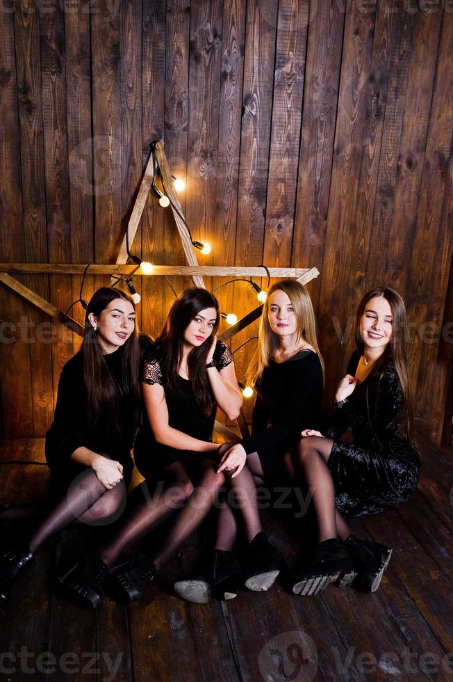quattro ragazze carine amiche indossano abiti neri contro una grande decorazione a stella di Natale su sfondo di legno. foto
