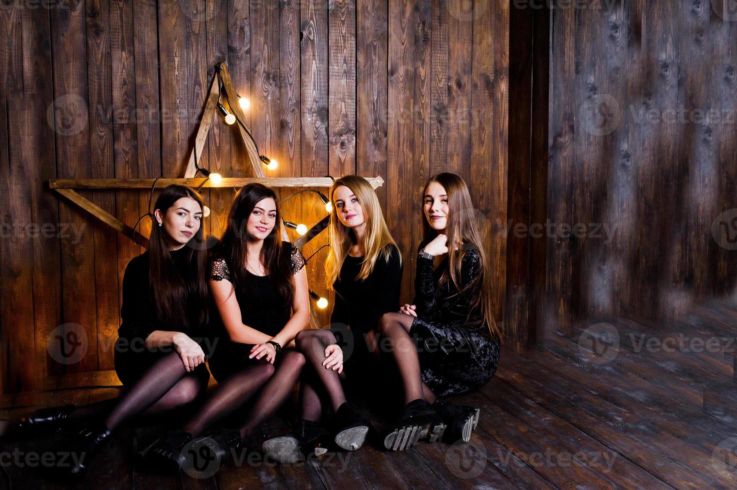quattro ragazze carine amiche indossano abiti neri contro una grande decorazione a stella di Natale su sfondo di legno. foto