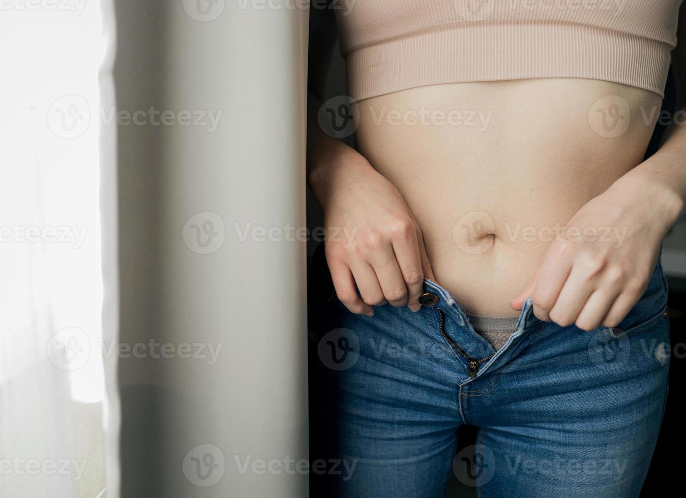 le mani delle donne si abbottonano i jeans foto