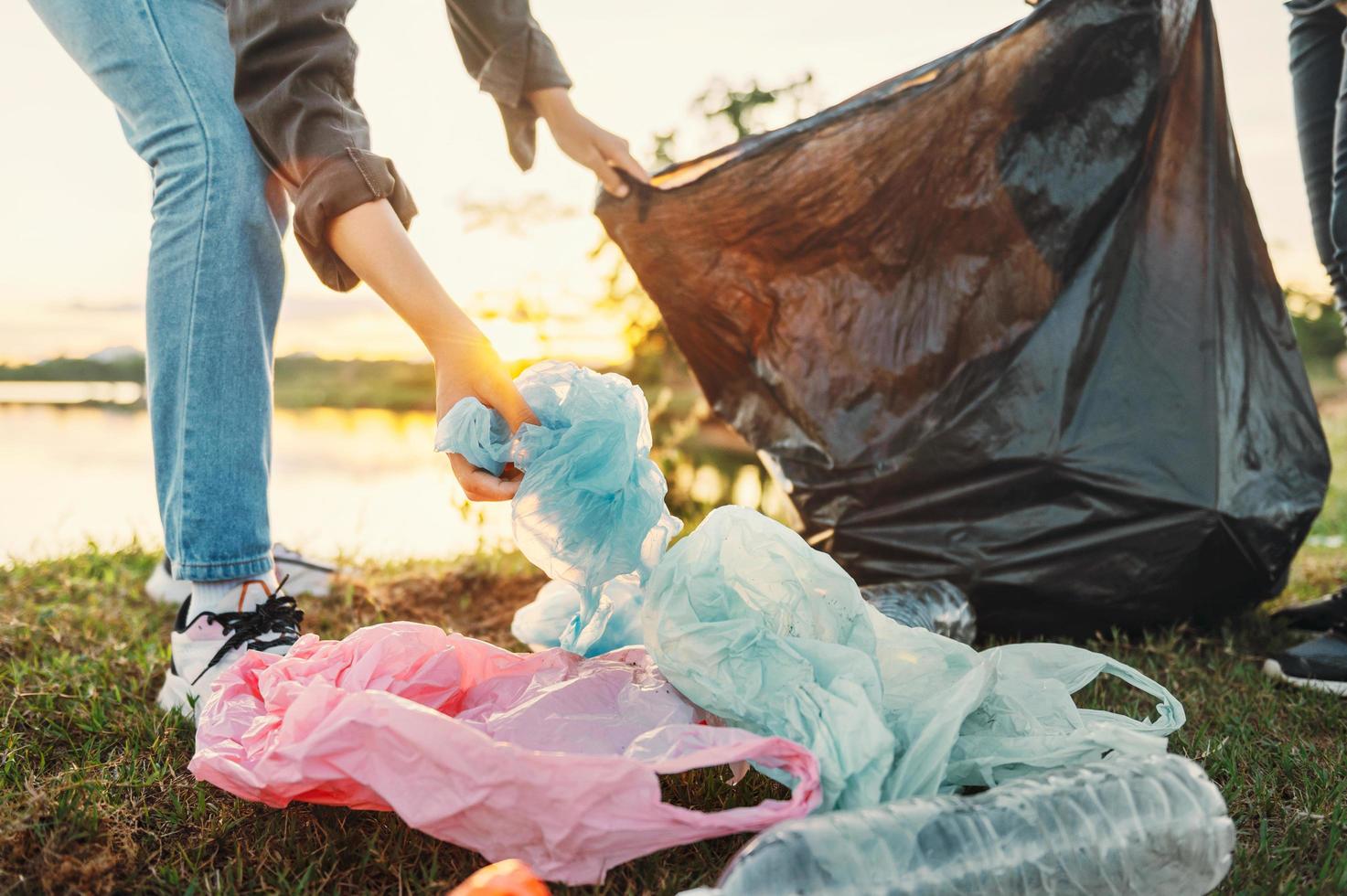 mano della donna che raccoglie la plastica dell'immondizia per la pulizia al parco foto