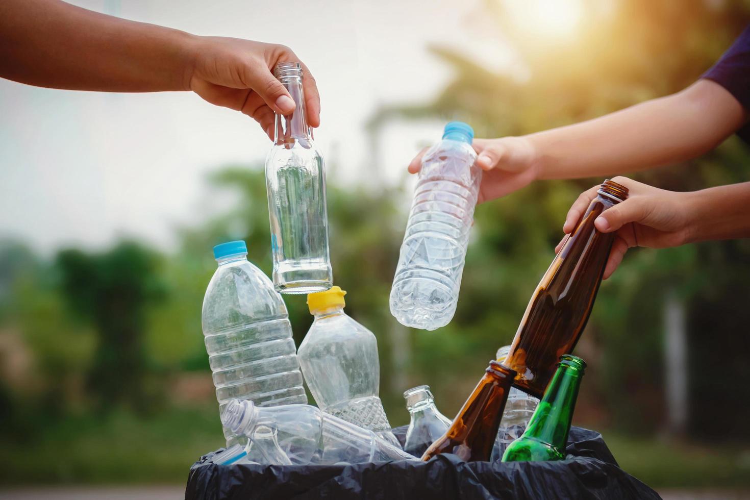 le persone tengono in mano una bottiglia di immondizia in plastica e vetro che mettono nel sacchetto di riciclaggio per la pulizia foto