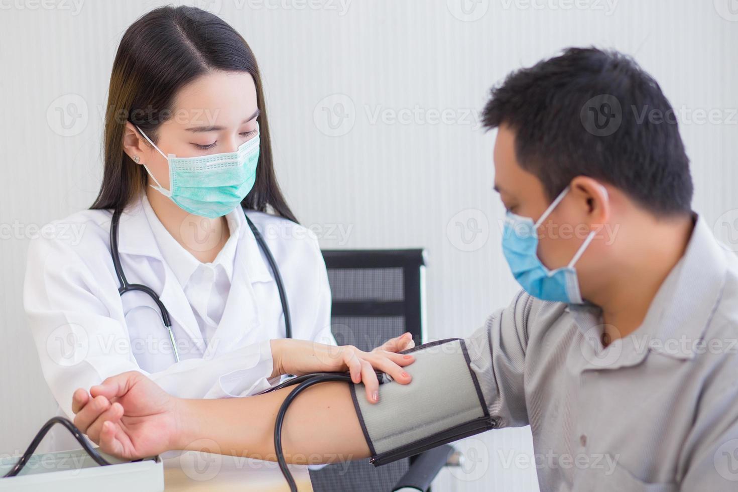 la dottoressa asiatica professionista usa un misuratore di pressione sanguigna con un paziente uomo per controllare la sua salute in ospedale. indossano una maschera medica per proteggere l'infezione del sistema respiratorio. foto
