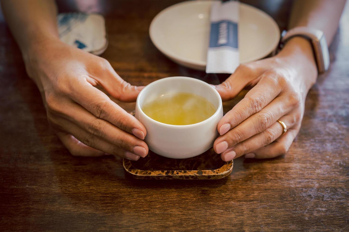 mani che tengono una tazza di tè verde caldo su un vassoio. foto