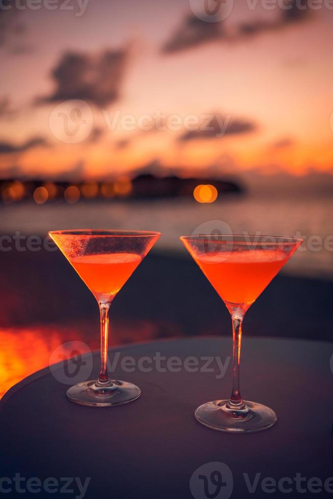 due cocktail drink con sfocatura persone festa in spiaggia e colorato cielo al tramonto sullo sfondo. stile di vita di lusso all'aperto, colori rilassanti e romantici, persone sfocate che fanno festa in una sera d'estate foto