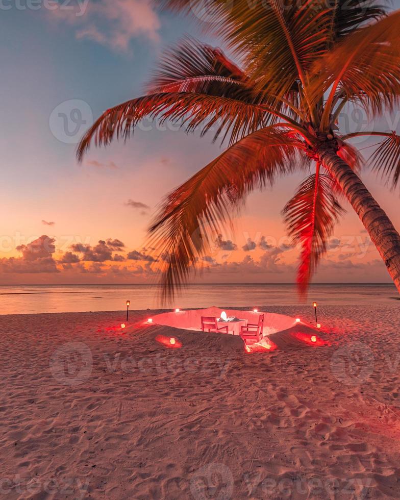 cena romantica in spiaggia con tramonto, candele con foglie di palma e tramonto cielo e mare. vista straordinaria, luna di miele o paesaggio per la cena di anniversario. orizzonte serale dell'isola esotica, romanticismo per una coppia foto