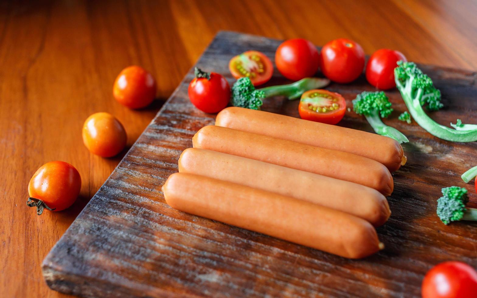 salsiccia cruda su un tagliere di legno con broccoli e pomodori foto