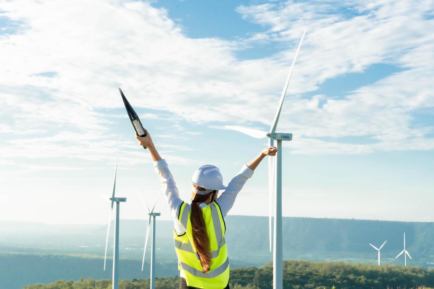 bella donna asiatica ingegnere in casco bianco che lavora con il documento presso una fattoria di energia rinnovabile. ispettore femminile che controlla il funzionamento delle turbine eoliche. Generatore sostenibile di energia, elettricità. foto