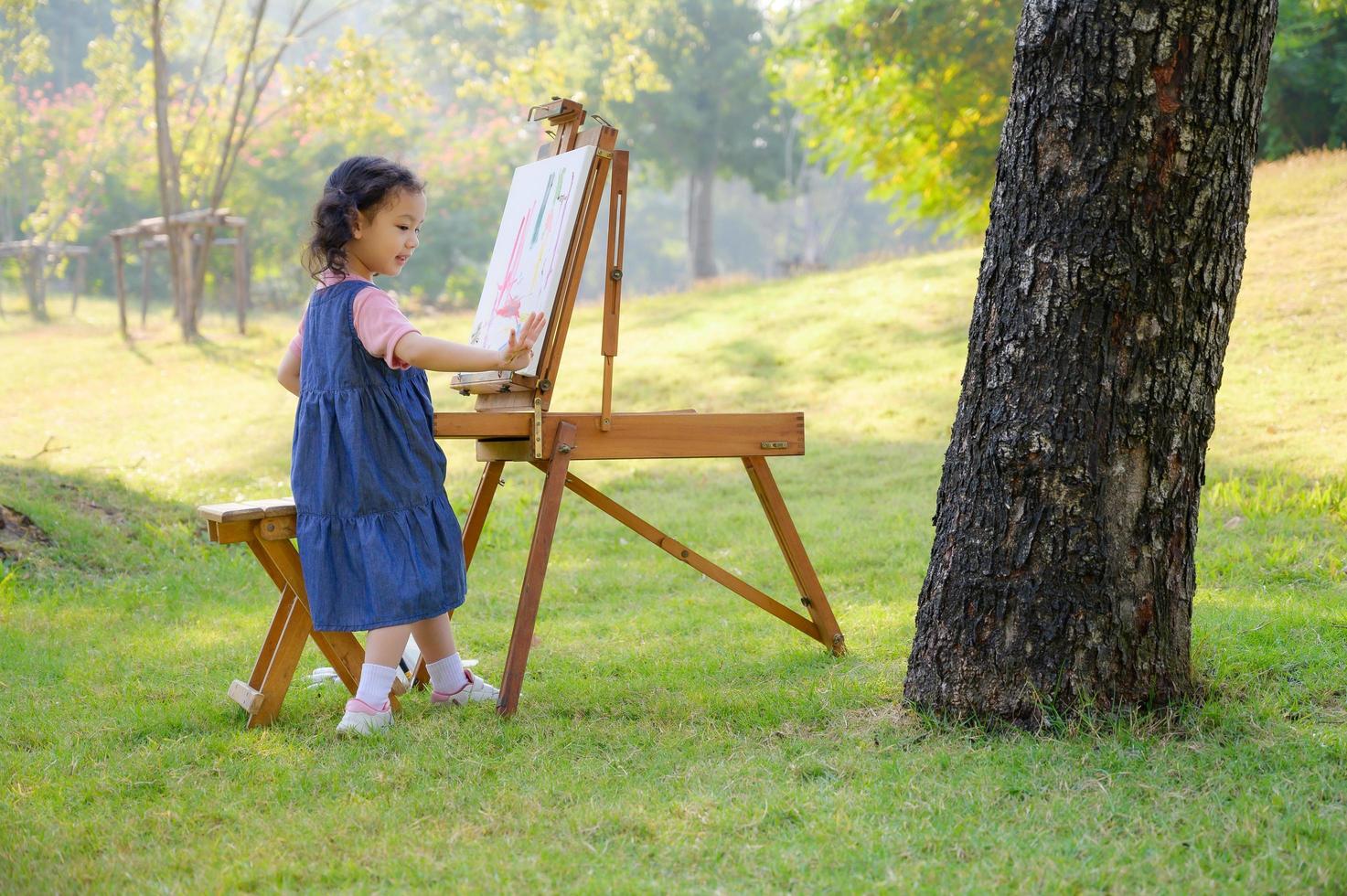 una bambina è in piedi sull'erba e dipinta sulla tela posta su un leggio da disegno foto