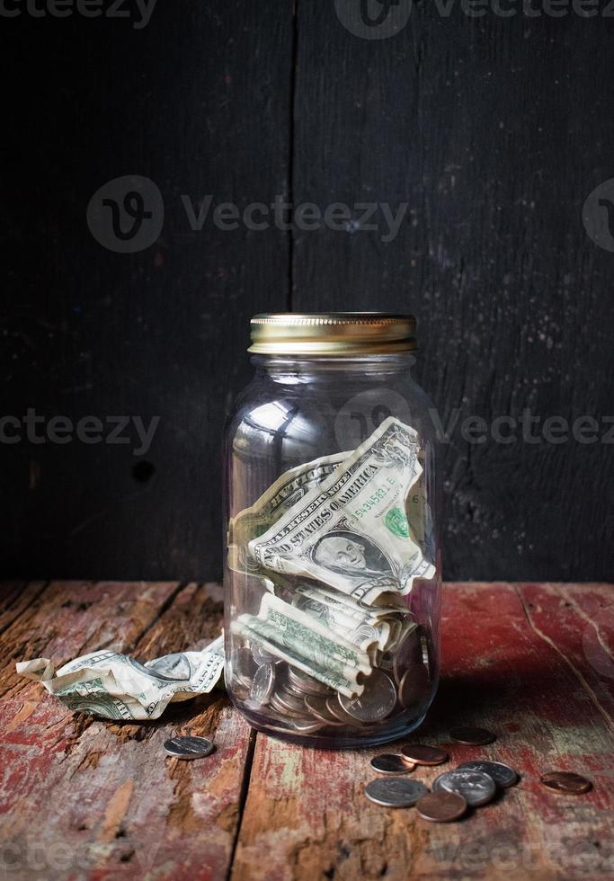 vaso di denaro con monete e banconote su tavola di legno rustica foto