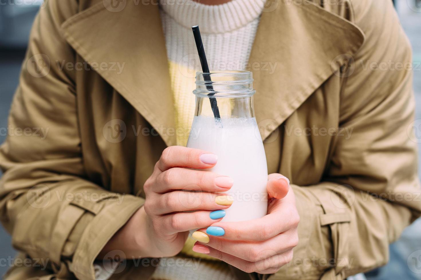 una giovane donna beve un frullato all'aperto da un elegante barattolo di vetro con una cannuccia foto