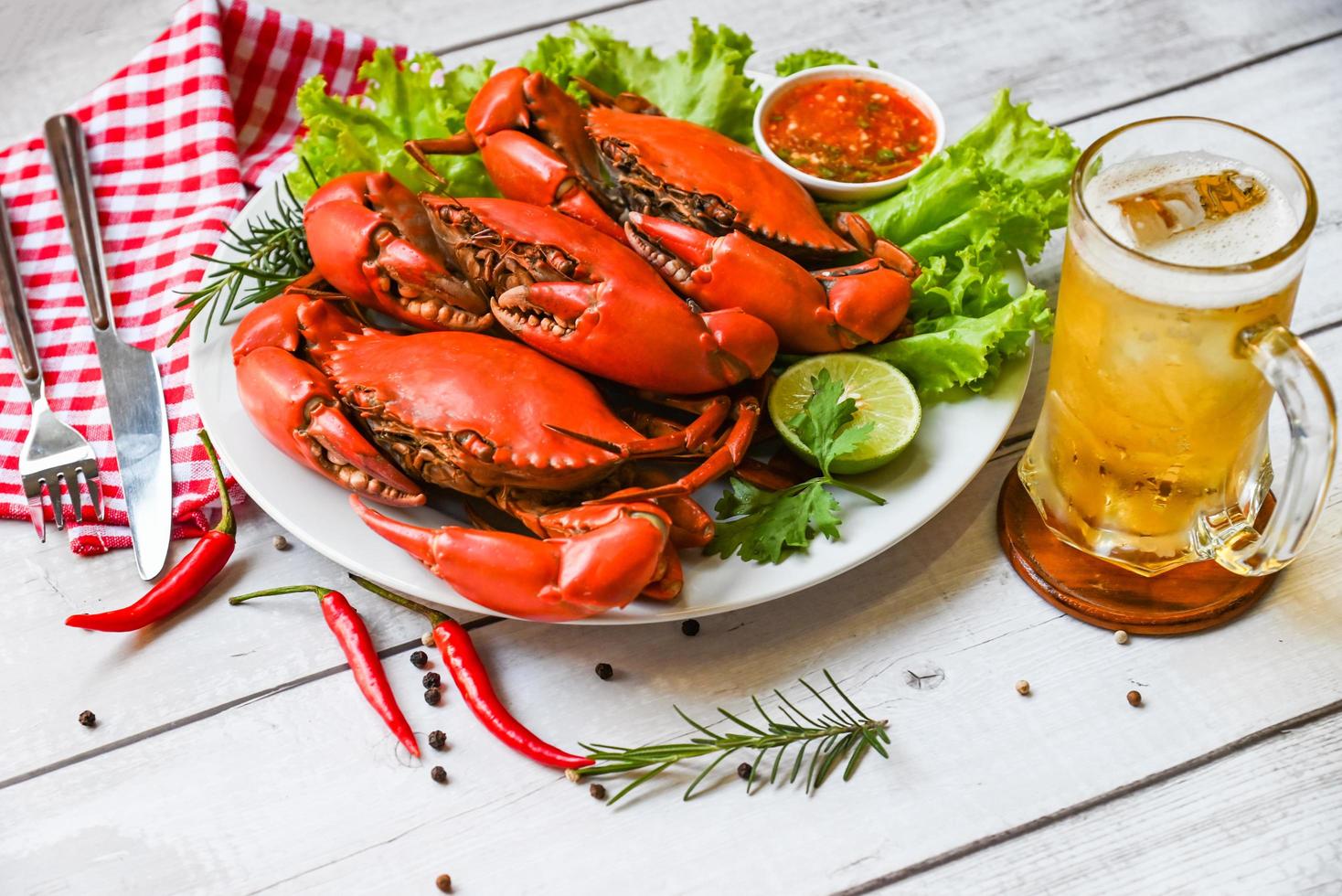 piatto di frutti di mare con erbe aromatiche spezie rosmarino limone lime insalata lattuga verdura, granchio fresco su piatto bianco salsa di frutti di mare e boccale bicchiere di birra, granchio cibo da cucinare granchio bollito o al vapore rosso al ristorante foto