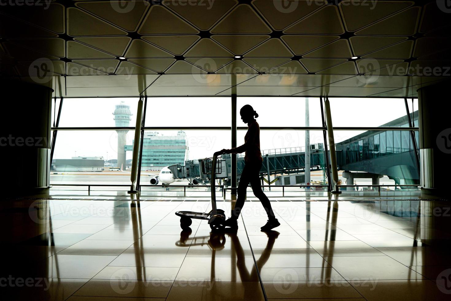 silhouette passeggero che cammina al terminal dell'aeroporto con carrello per i bagagli foto