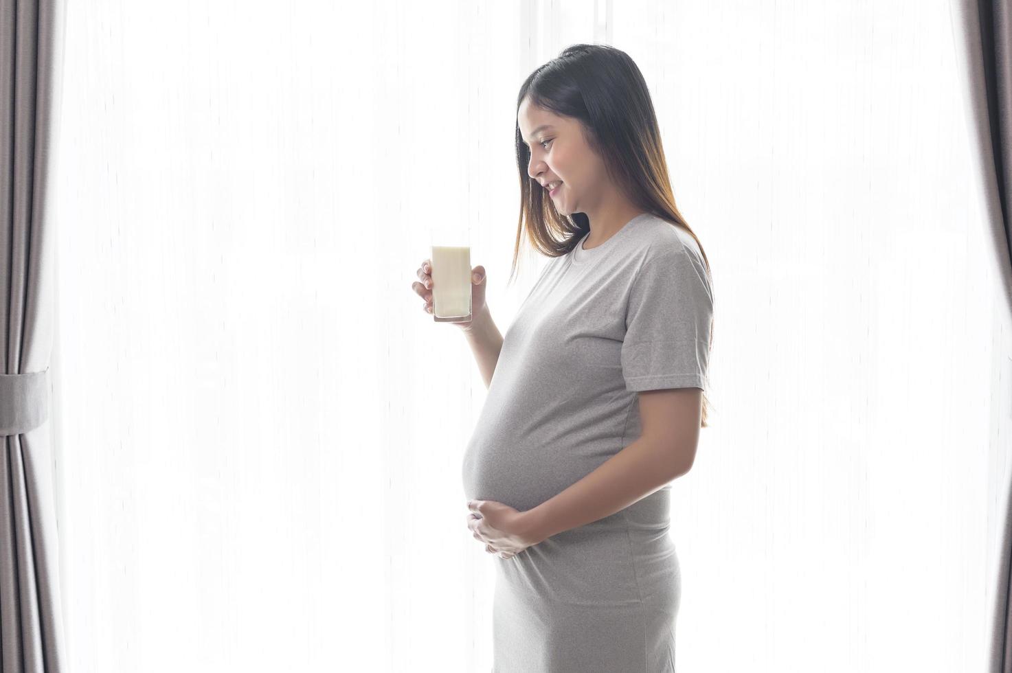 giovane donna incinta che beve latte a casa, assistenza sanitaria e gravidanza foto