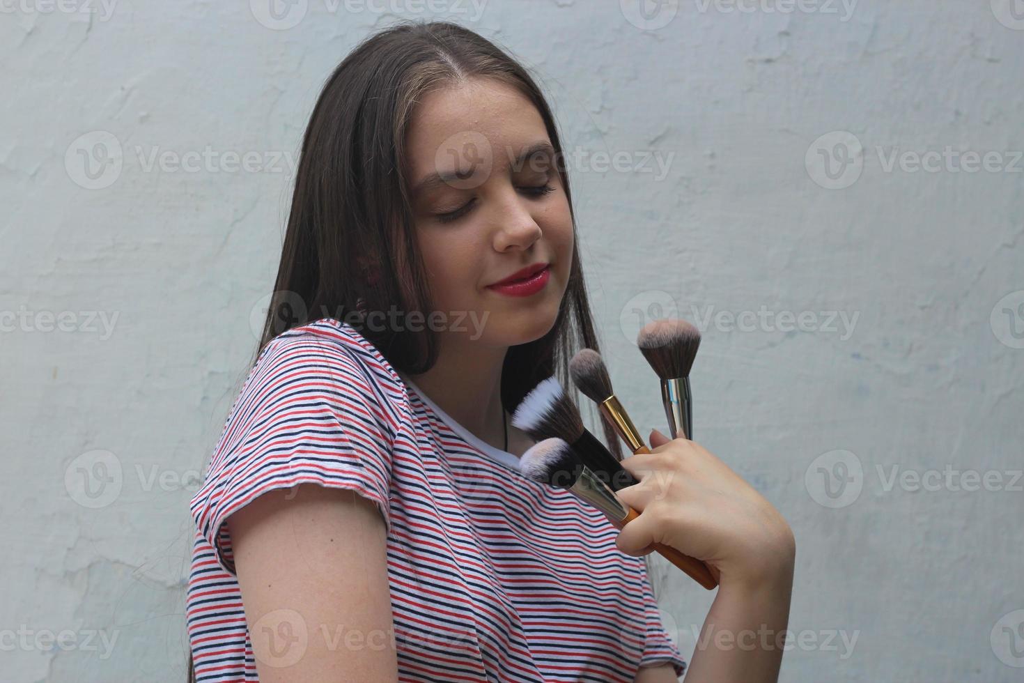 un'adolescente si trucca a casa, un'adolescente con i capelli scuri tiene i pennelli da trucco foto