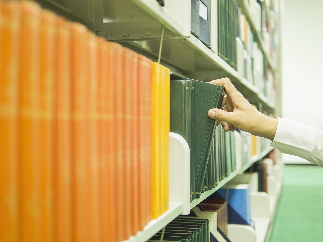 l'uomo sta selezionando il libro dallo scaffale di una libreria foto